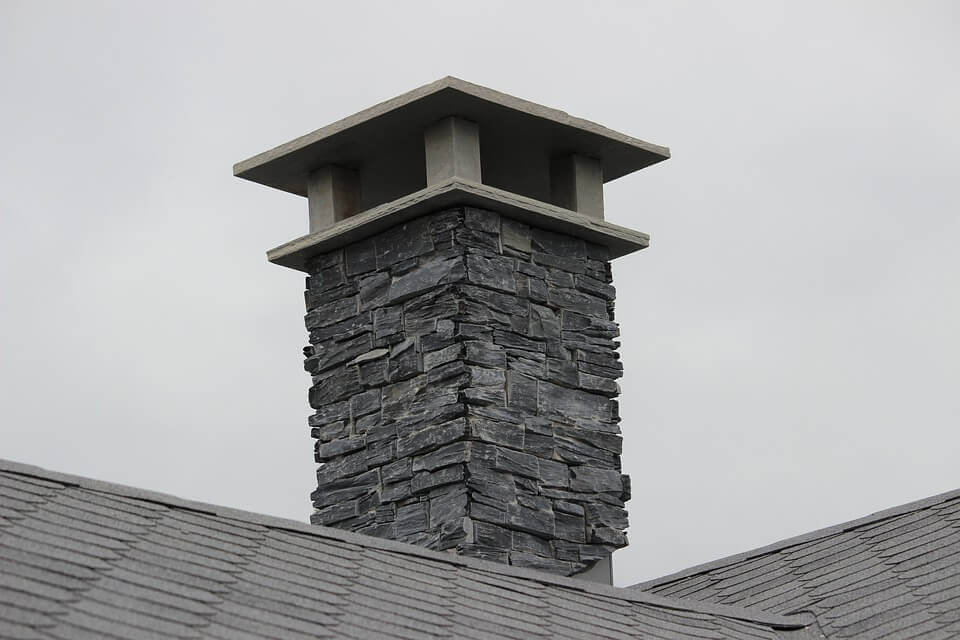 Grey brick chimney with new chimney cap. Roof seen in forefront