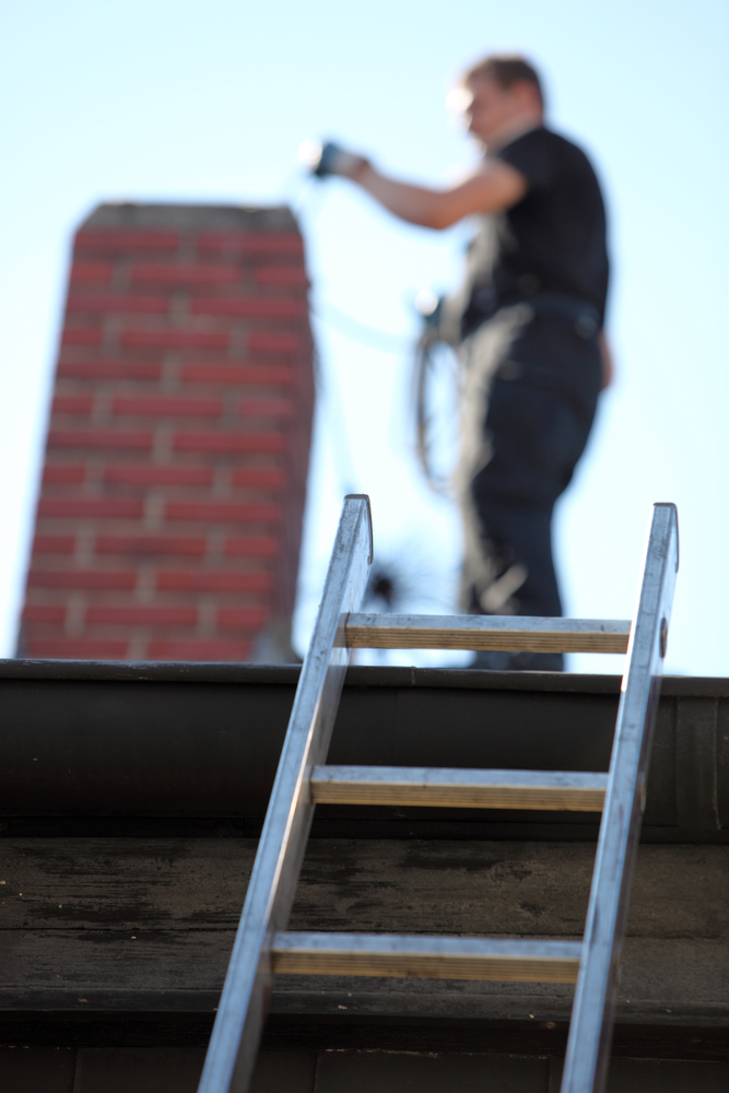 Chimney sweep on roof with ladder leaning against home.  He is doing an inspection.